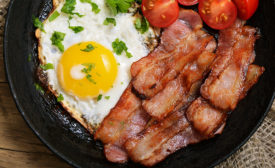 Appetizer fried egg with bacon in frying pan, top view