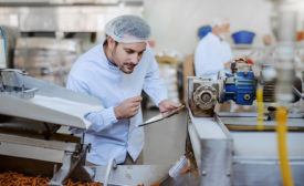 supervisor evaluating quality of food in food plant while holding tablet