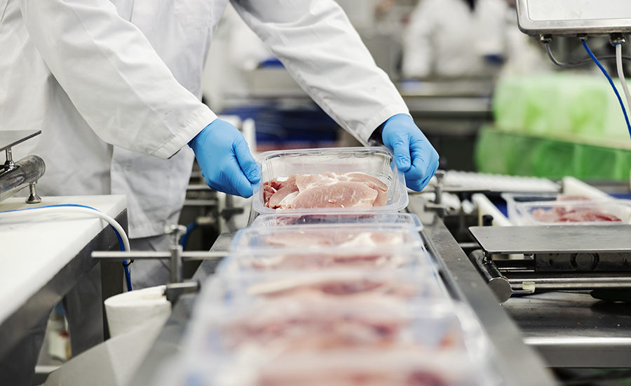 Close up of a meat industry worker gathering packed meat on a conveyor belt.