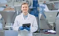 Young Male Quality Supervisor or Food Technician is Inspecting the Automated Production at a Dumpling Food Factory. Employee Uses a Tablet Computer for Work. He Looks to the Camera and Smiles.