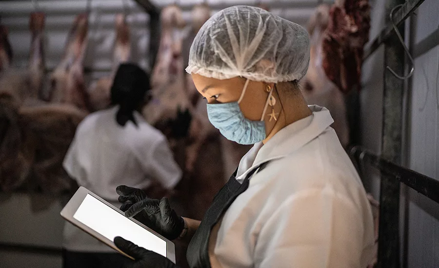 Female butcher using digital tablet with face mask at cold storage