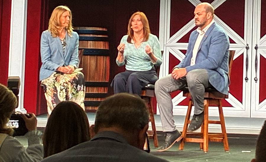 Three speakers on a stage with a red and white barn backdrop.