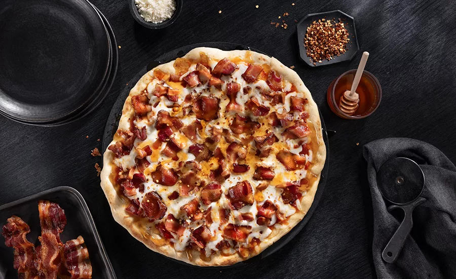 Overhead shot of a whole pizza on a table with a jar of honey beside it.