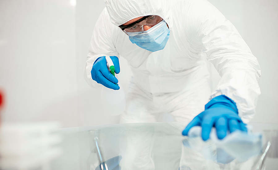person in PPE sanitizing surfaces