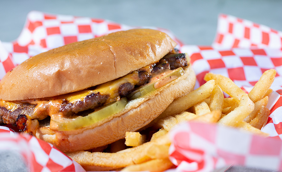 A cheeseburger with pickles, special sauce, and fries in a basket with red and white paper wrapper and tray.