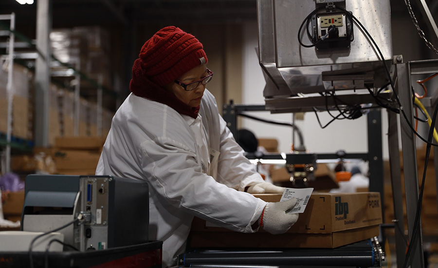 Worker labeling 'IBP Pork' boxes in a factory setting.