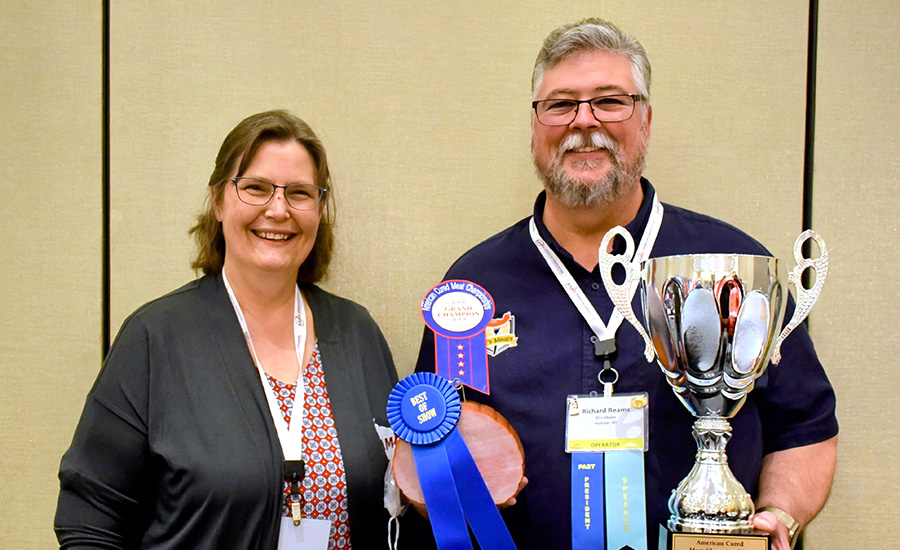 2024 AAMP Best of Show winners, the woman on the left holding a ham with a "Best of Show" ribbons attached, the man on the right is holding a silver cup trophy.