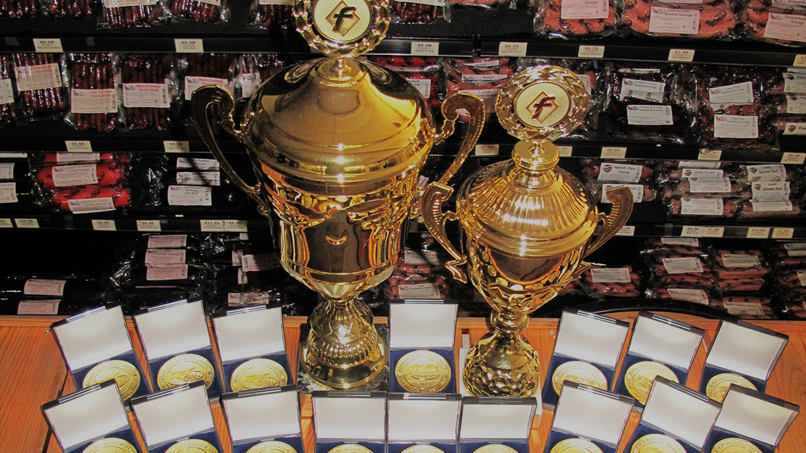 Two golden trophies and rows of gold, silver, bronze medals for meat product quality.