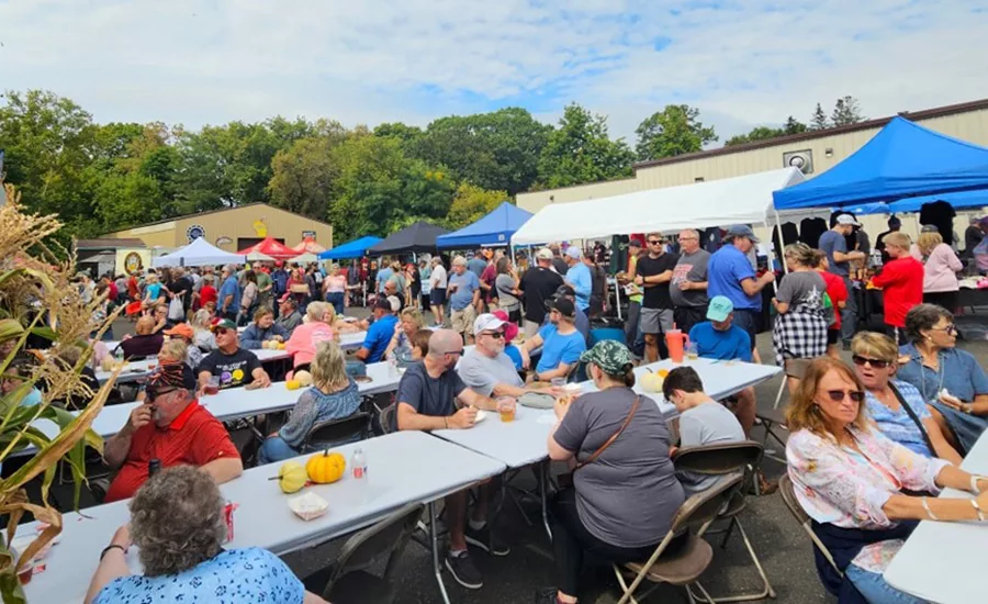 People seated at tables next to pop-up tents at an outdoor event.