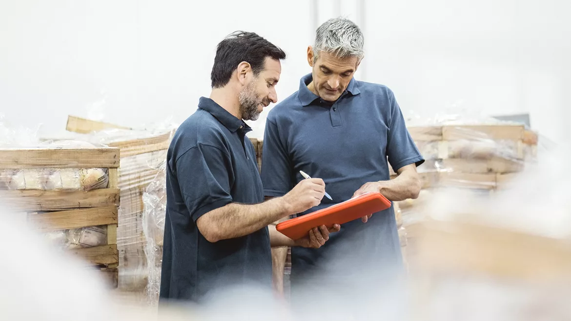 Two men looking over a work order surrounded by pallets of products.