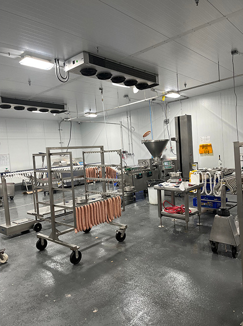 Sausages hanging on a rack next to machinery.