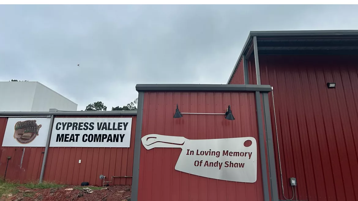 Cypress Valley Meat Company building signage along with a large sign in the shape of a meat cleaver with a text cutout that says "In Loving Memory of Andy Shaw".