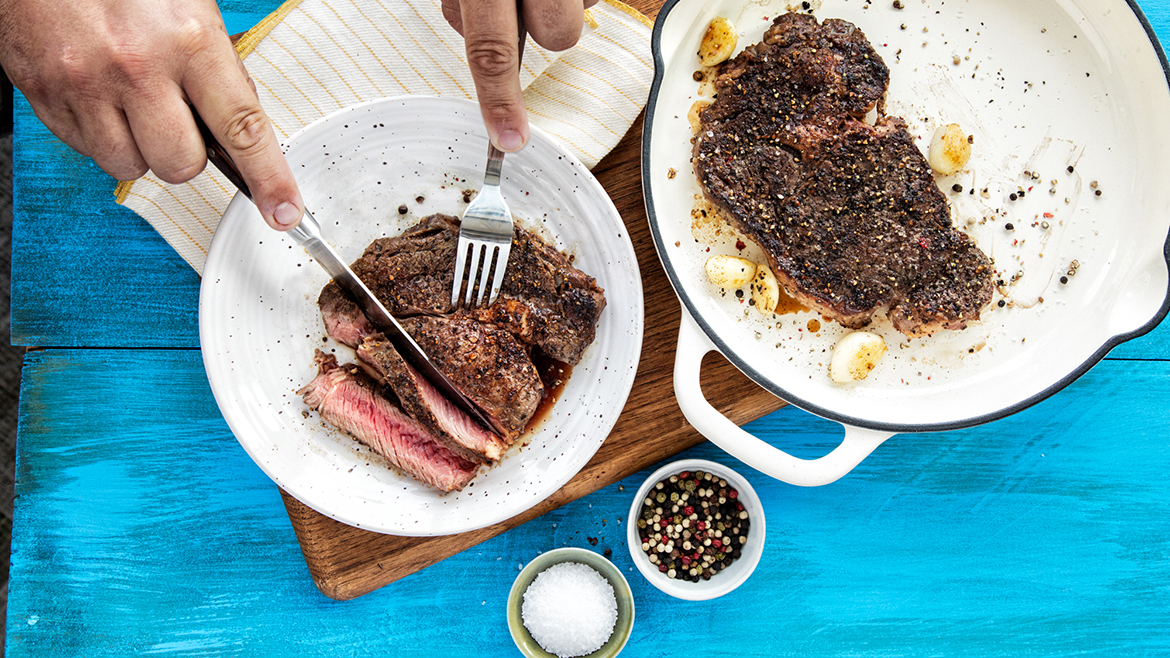 A cooked Verde Farms ribeye steak on a platter and a smaller piece being sliced on a plate.