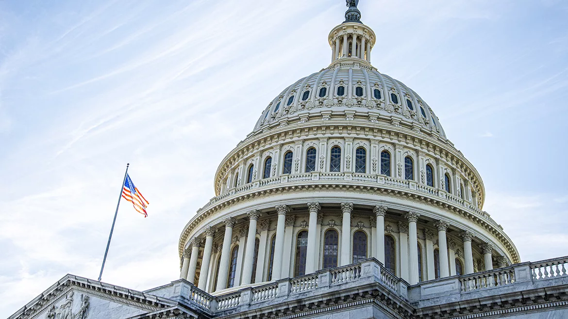 The U.S. flag on a flagpole and the dome of the U.S. Capitol Building in Washington D.C.