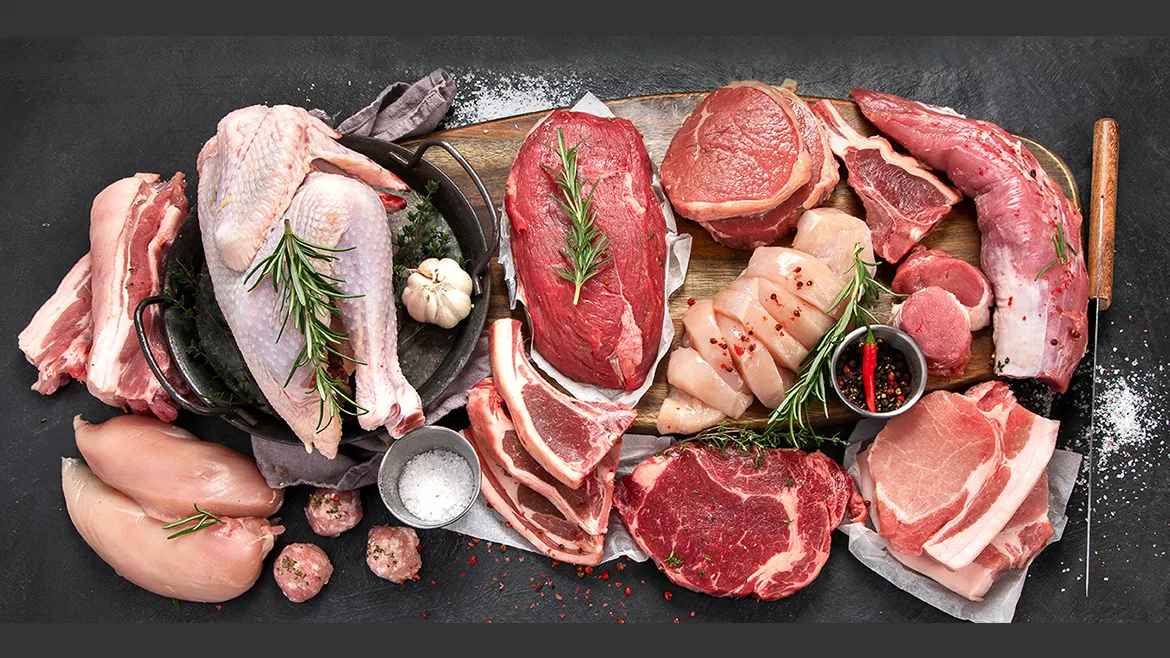 Several cuts of beef, pork and chicken on a wooden board, cast iron pan and salt.