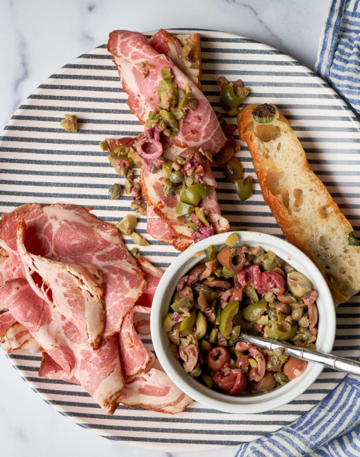 Fra Mani Spicy Capicollo Focaccia Olives and capers salad on a striped plate.