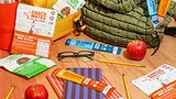 Various new Primal snack sticks on a table amongst pencils, apples, a pair of glasses, lunch bags and a water bottle.