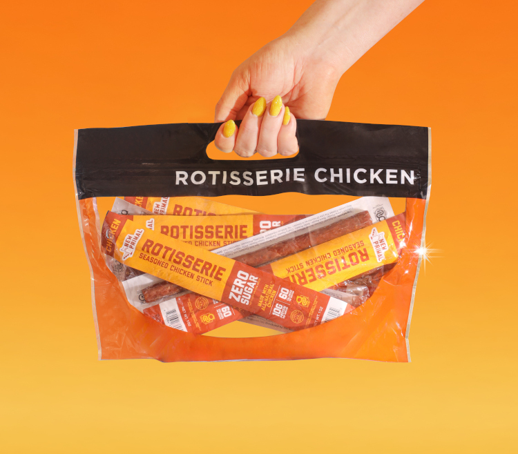 A hand is carrying a plastic back with a handle that says 'ROTISSERIE CHICKEN'. The contents are a bunch of Primal Rotisserie Seasoned Chicken Sticks.