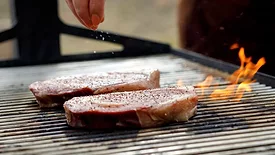 two thick steaks grilling over an open flame 