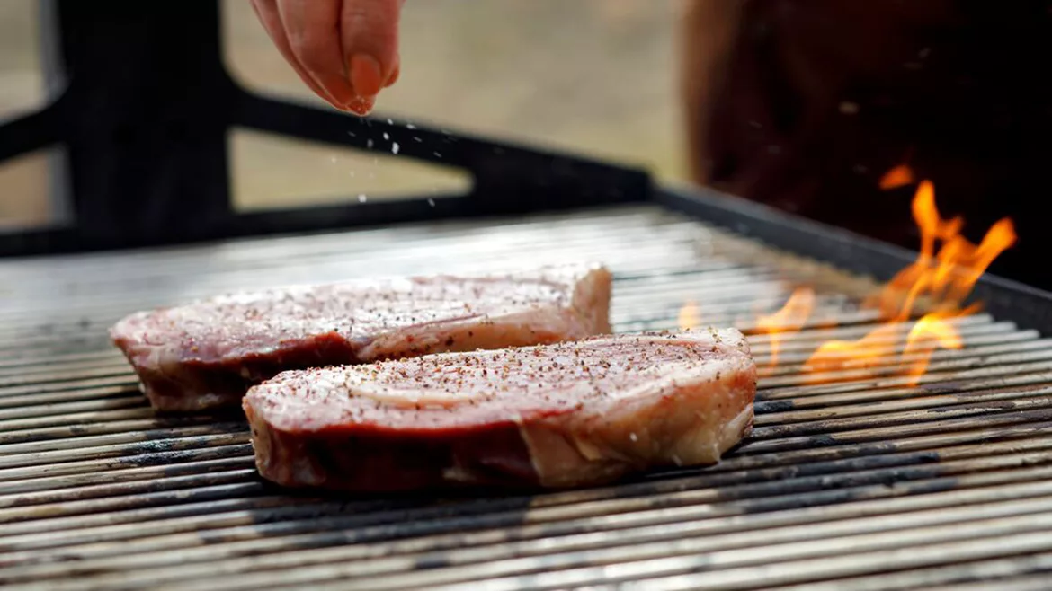 two thick steaks grilling over an open flame 