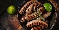 Grilled sausages Overhead view of grilled sausages in a skillet with thyme sprigs and lime wedges.