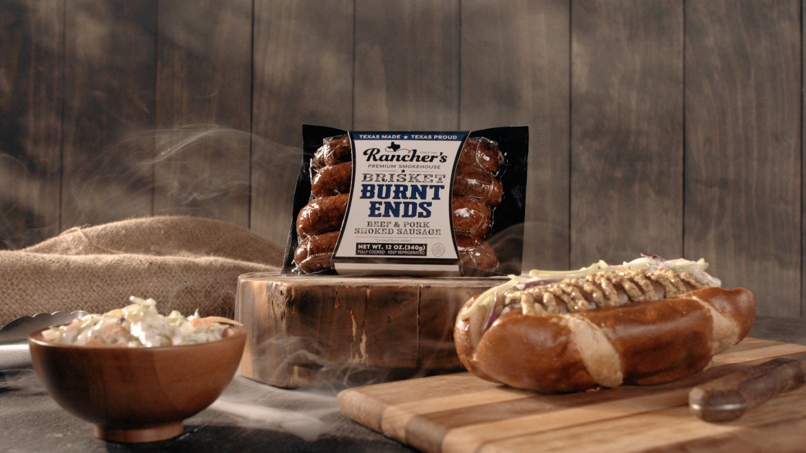 Rancher's Brisket Burnt Ends Smoked Sausage package with hot dog and coleslaw on a rustic background.
