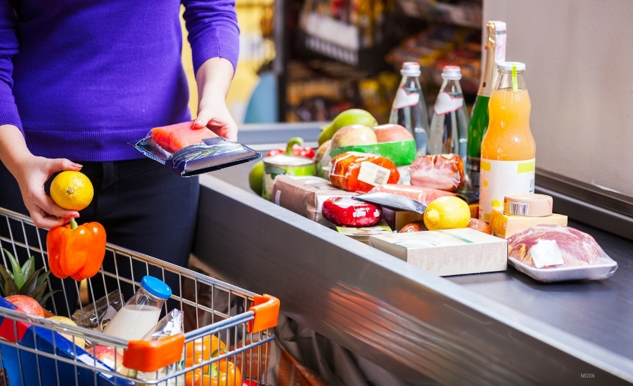 A cropped image of a woman in a purple blouse is checking out groceries.