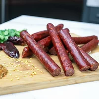 Seasoned sausages stacked on a wooden board along with various seeds, peppers and herbs.